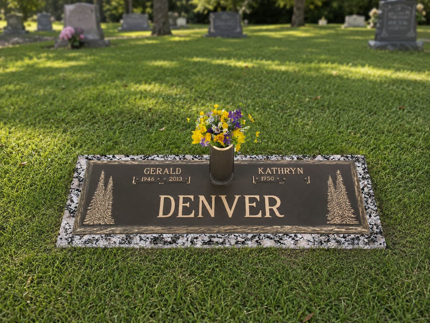 A bronze grave marker with a pine emblem sitting in a cemetery field.